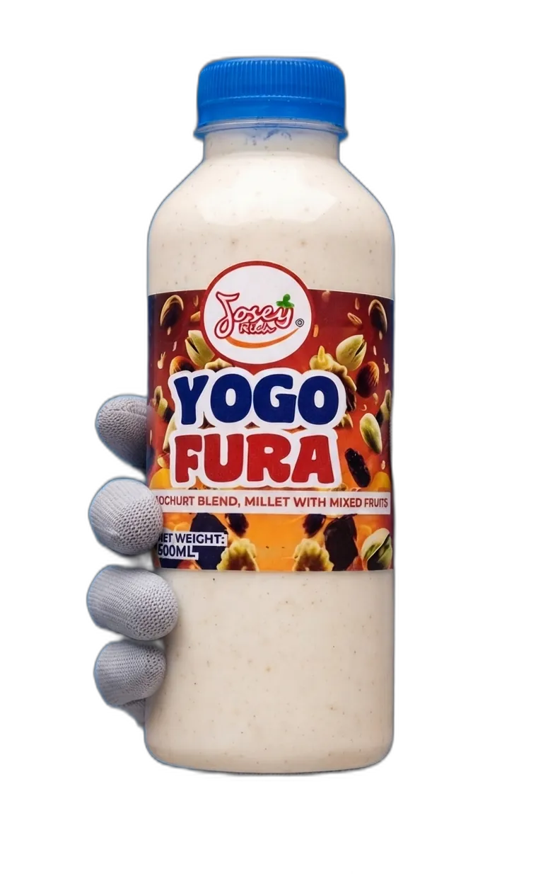 A gloved hand holding a 500 ml bottle of Josey Rich Yogo Fura, its amber label printed with dates, nuts and pistachios above the words YOGHURT BLEND, MILLET WITH MIXED FRUITS.